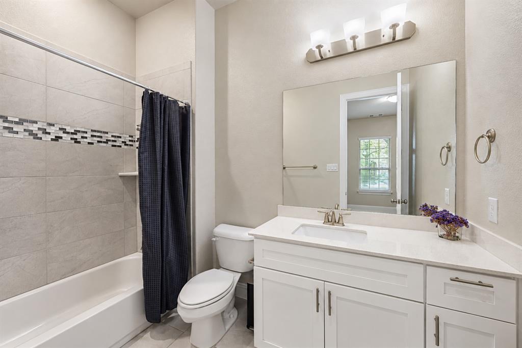 Bathroom featuring a white vanity with an integrated sink, a large wall-mounted mirror, a three-light vanity fixture, a toilet, and a tub with tile surround and decorative accent band