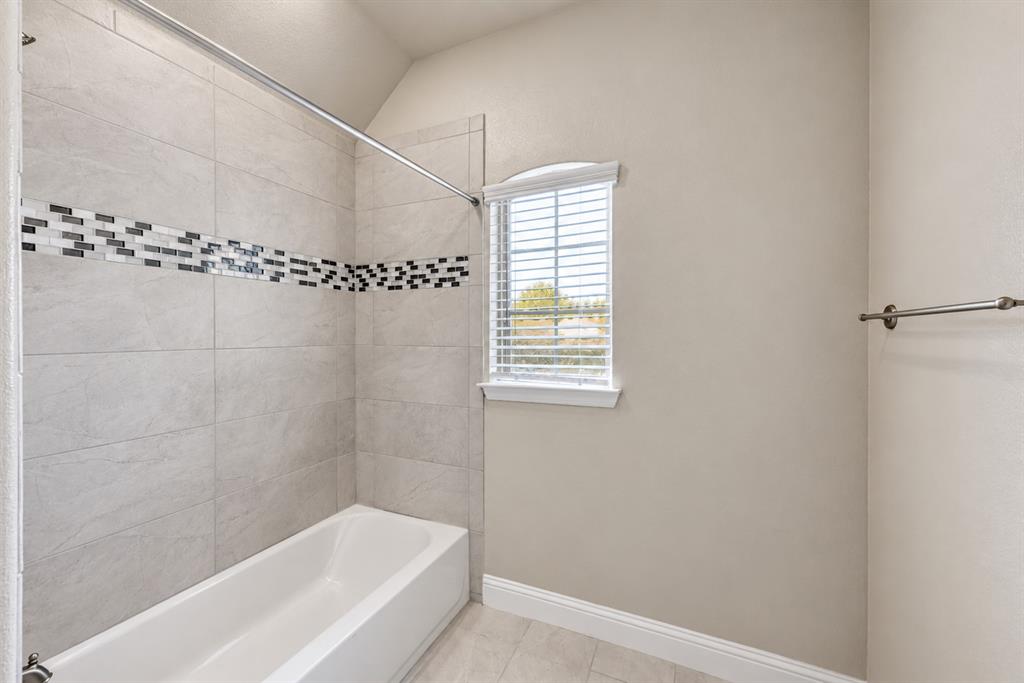 Bathtub with floor-to-ceiling tile surround, mosaic tile accent, and a window with blinds