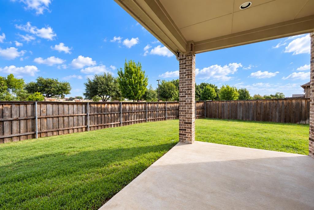 Expansive backyard featuring a manicured lawn, full privacy fencing, and a covered concrete patio with brick columns