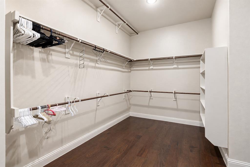 Walk-in closet with dark wood-finish flooring, white built-in shelving, and multiple clothing rods