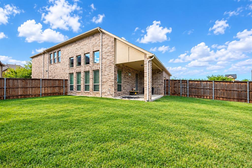 Expansive green lawn, wood fence, brick exterior, covered patio, and multiple windows