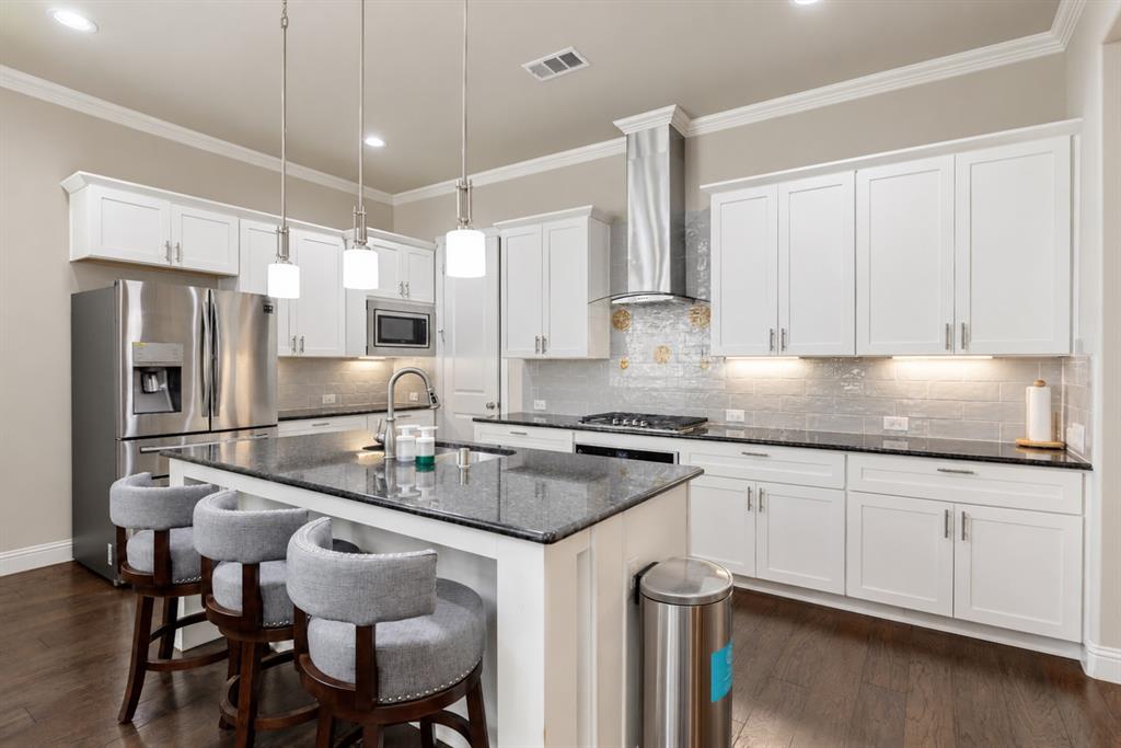 Kitchen featuring white cabinetry, dark stone countertops, stainless steel appliances, a center island with pendant lighting, and wood-finish flooring