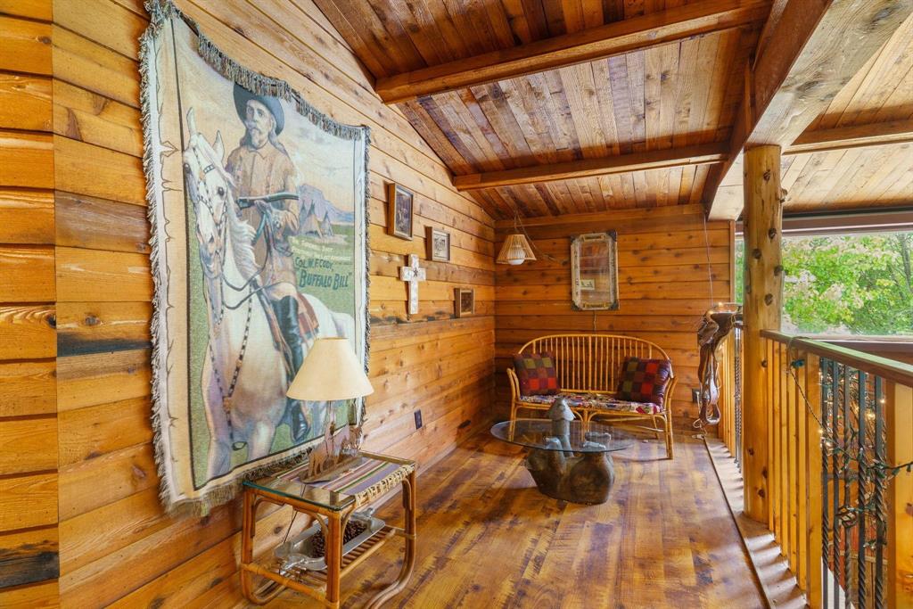 Log-paneled walls and ceiling with exposed timber support beams, natural wood-finish flooring, and a decorative metal spindle railing