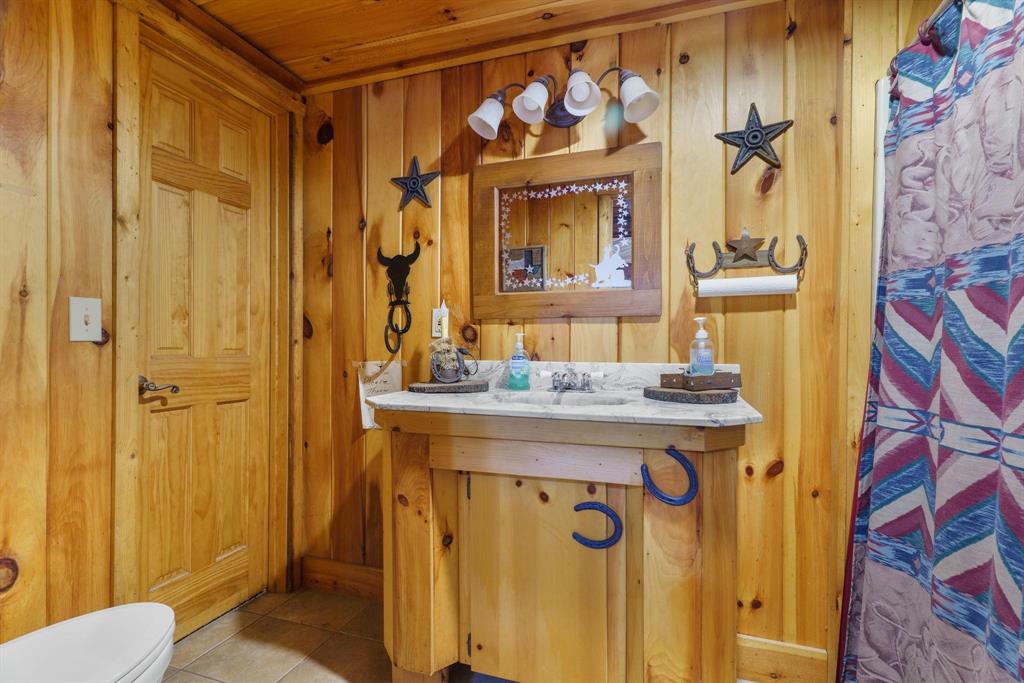 Bathroom featuring vertical wood paneled walls, a custom wood vanity with a stone countertop, an integrated sink, a matching wood-framed mirror, and a four-light fixture