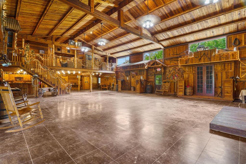 Expansive open-concept interior featuring exposed wooden ceiling beams, natural wood wall paneling, tiled flooring, a built-in wooden staircase with matching railings, and glass-paneled double doors