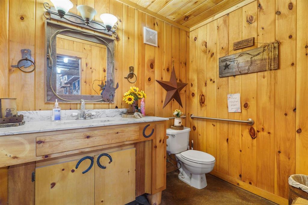 Bathroom featuring knotty pine wall paneling, a custom wood vanity with a stone countertop, an integrated sink, and an attached three-light fixture