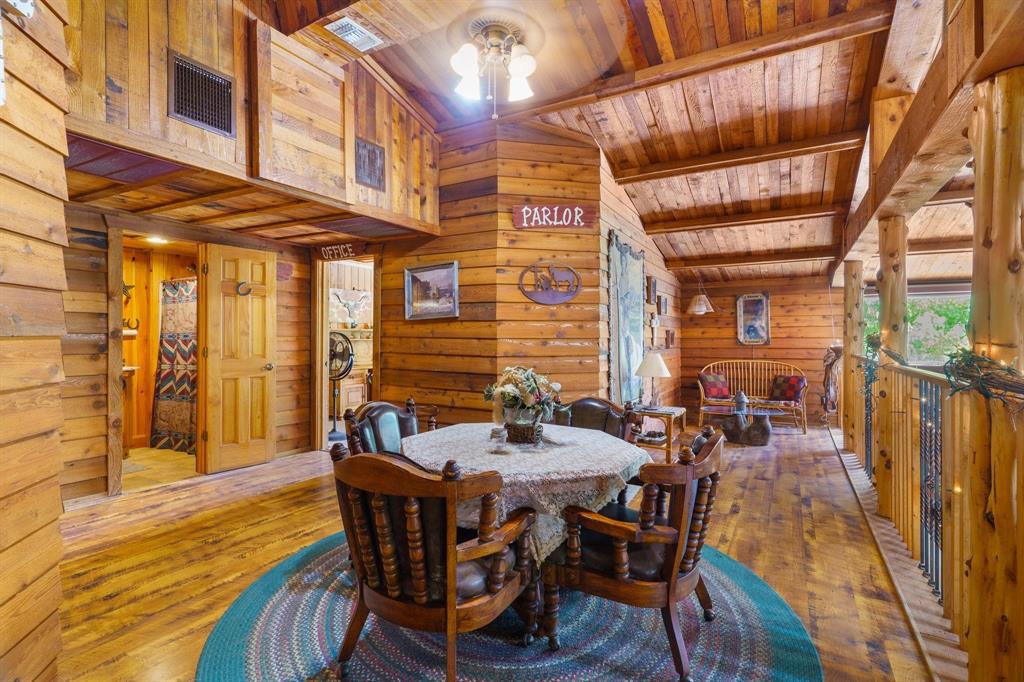 Interior space featuring rustic log-style wall paneling, vaulted ceilings with exposed timber beams, wood-finish flooring, and a decorative metal railing