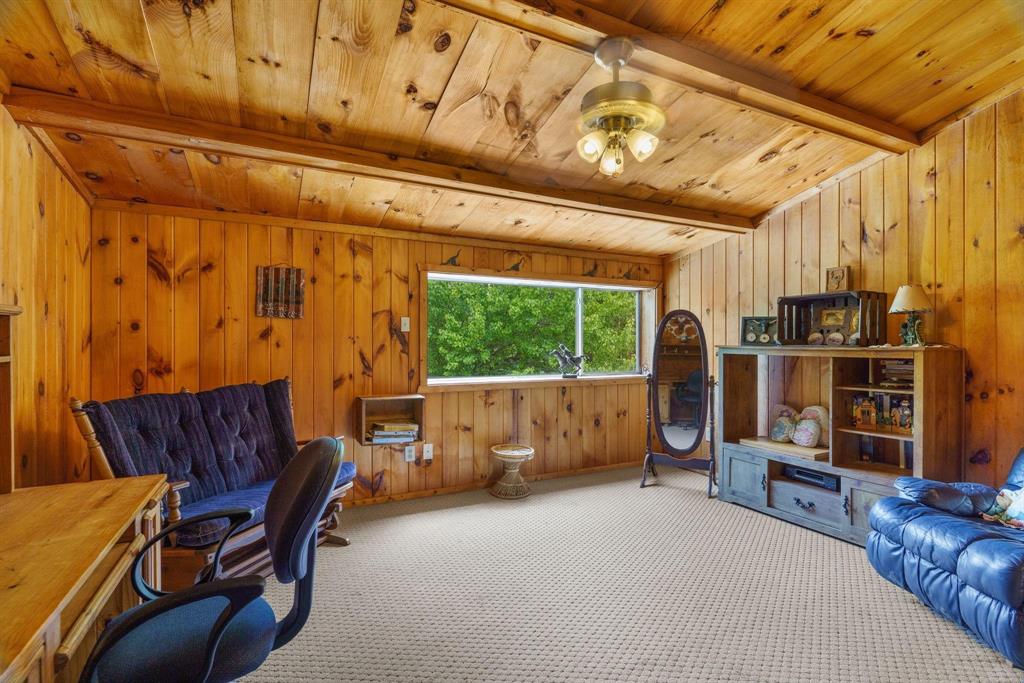 Wood-paneled walls, vaulted ceiling with exposed wood beams, large picture window, and ceiling-mounted light fixture with frosted glass shades