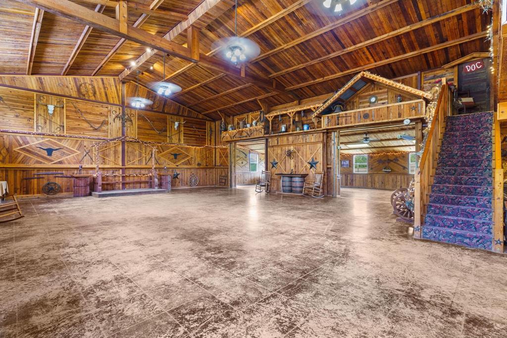 Expansive open-concept interior featuring vaulted wood-paneled ceilings with exposed rafters, full-height wood wall paneling, polished concrete flooring, and a built-in elevated loft structure