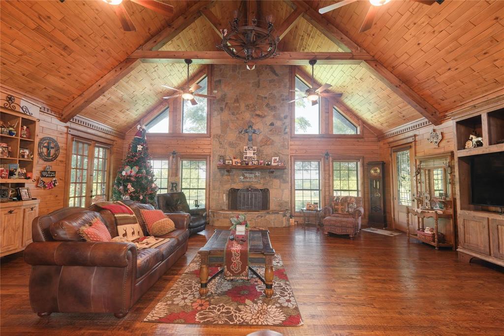 Vaulted ceiling with exposed timber beams and wood-plank paneling, floor-to-ceiling stone fireplace, built-in cabinetry, wood-finish flooring, and multi-pane windows