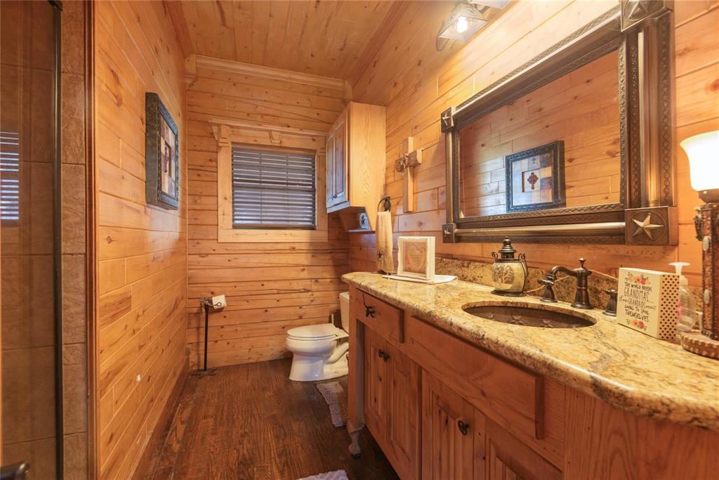Wood-paneled walls and ceiling, stone-finish vanity countertop with an integrated basin, custom wood cabinetry, and a large decorative wall-mounted mirror