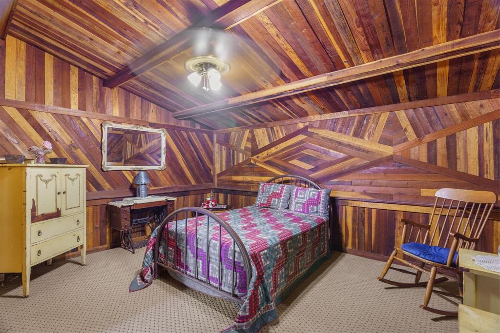 Geometric wood-paneled walls and vaulted ceilings featuring exposed wood-plank finish, wall-mounted mirror, and central multi-bulb ceiling fixture