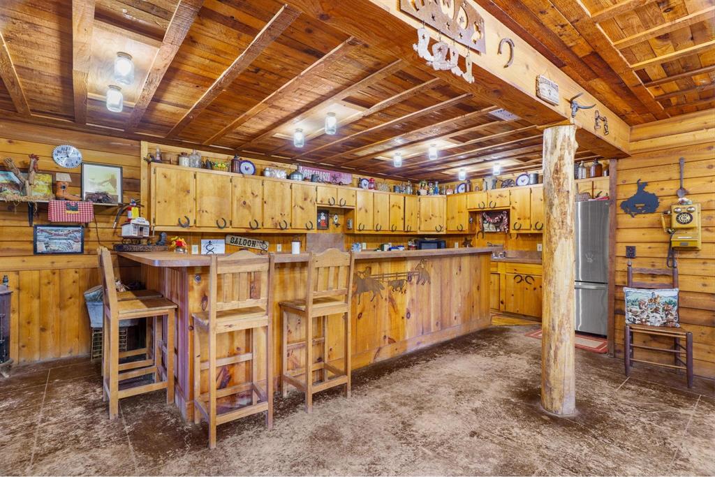 Rustic bar area featuring knotty pine wall paneling, exposed beam ceiling, built-in wooden cabinetry, custom wood bar top, and a structural log pillar