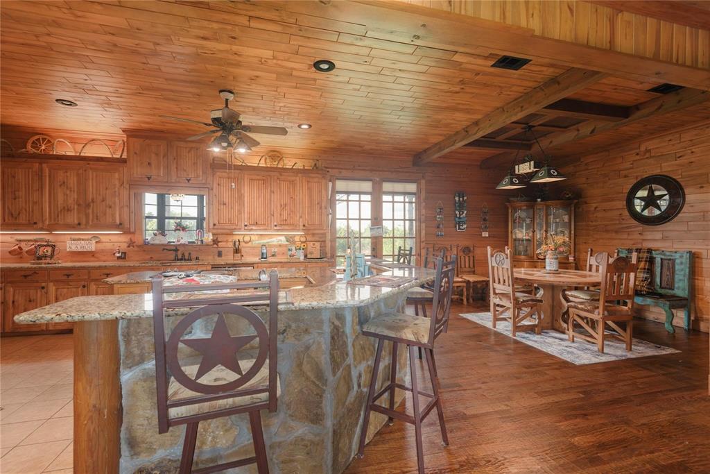 Kitchen featuring wood-paneled walls and ceilings, stone-faced kitchen island with a stone countertop, wood-finish cabinetry, and wood-finish flooring