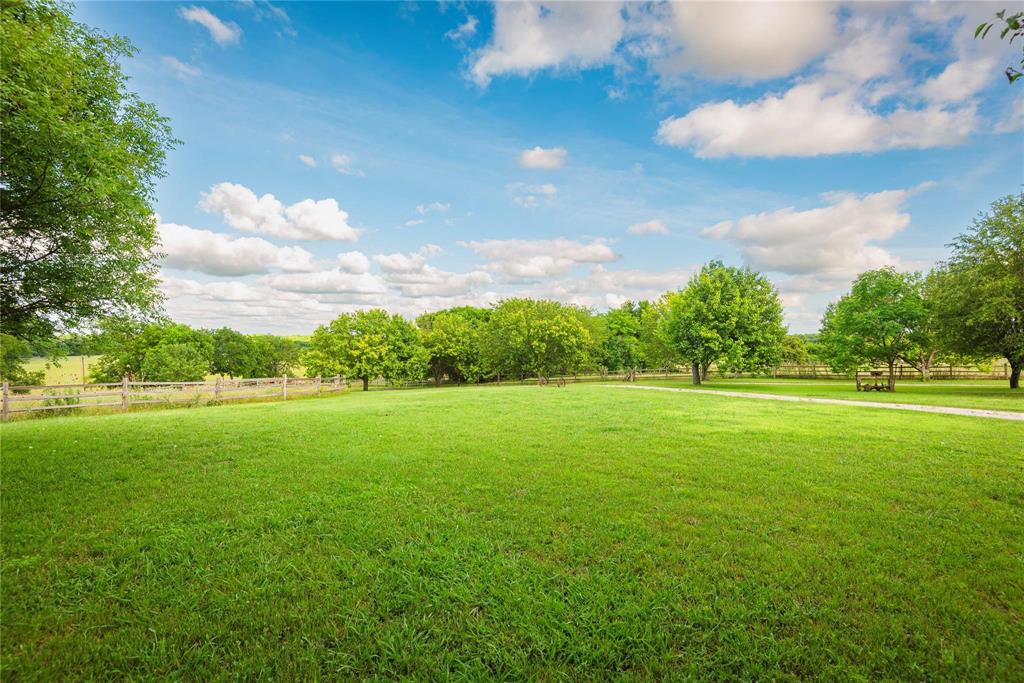 Expansive grounds featuring a manicured lawn, mature trees, split-rail perimeter fencing, and a gravel pathway