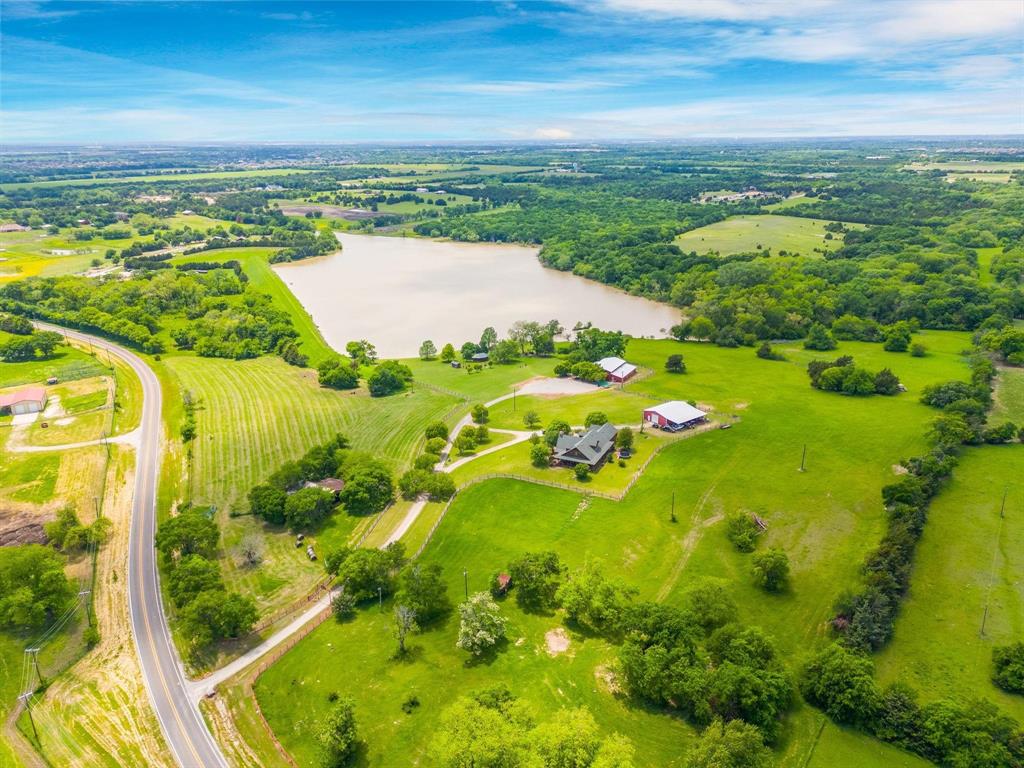 Aerial perspective of acreage featuring a private pond, expansive green pastures, mature trees, and multiple outbuildings
