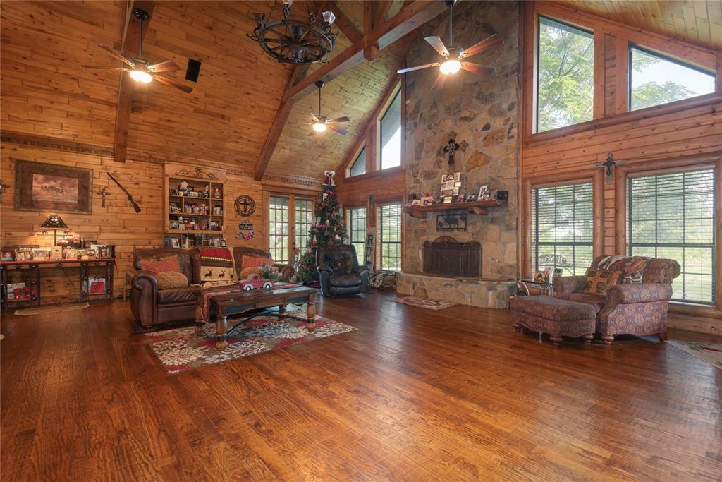 Vaulted wood-paneled ceiling with exposed beams, floor-to-ceiling natural stone fireplace, wood-finish flooring, multi-pane windows, and built-in wooden shelving