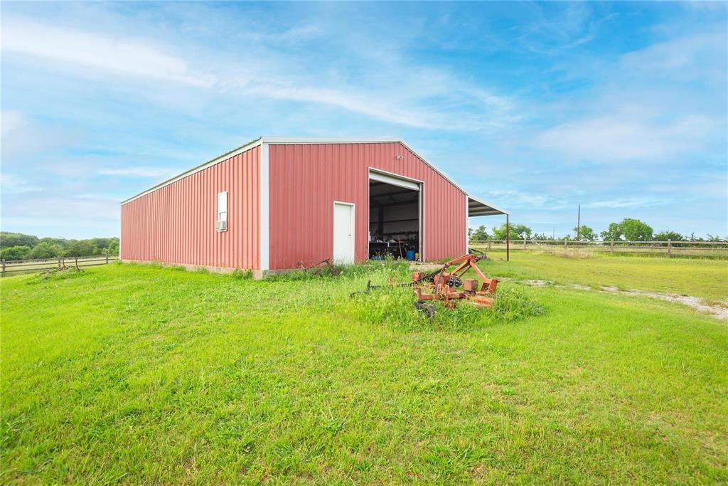 Detached metal workshop featuring a gable roof, large sliding door, and open-sided lean-to structure situated on a grass lot