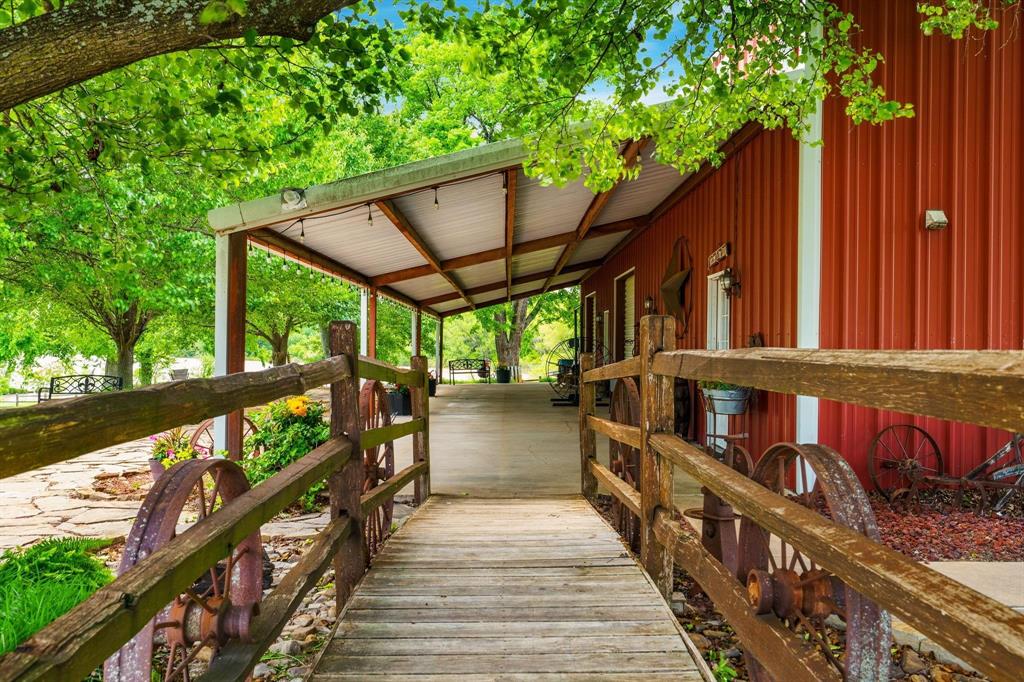 Covered porch with exposed wood rafters, metal siding exterior, wood-plank walkway, and rustic timber-rail fencing