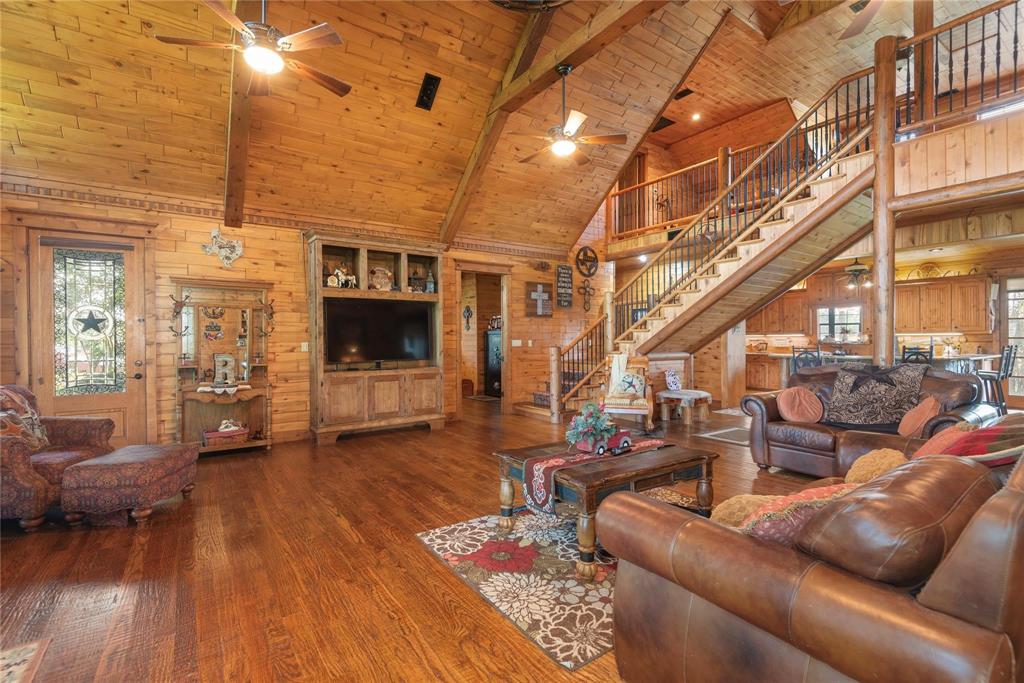 Vaulted ceilings with exposed timber beams, wood-plank wall paneling, built-in media cabinetry, wood-finish flooring, and an open staircase featuring metal balusters