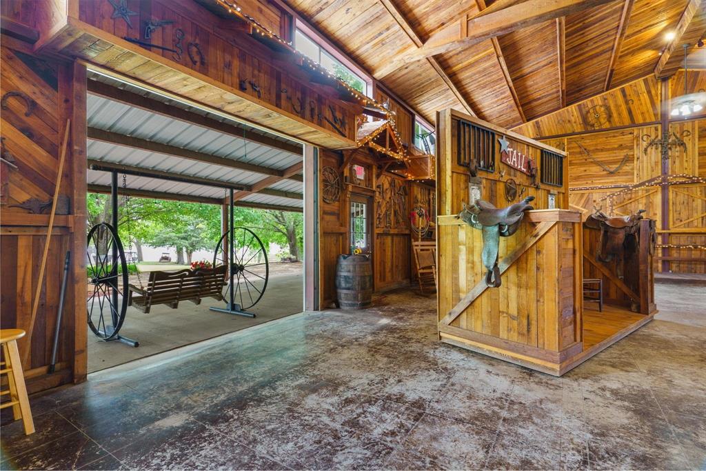 Interior space featuring extensive wood-paneled walls and exposed timber ceiling beams, concrete flooring, and a large opening to a covered outdoor area