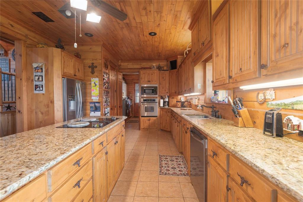 Kitchen featuring solid wood cabinetry, stone-surface countertops, built-in double wall ovens, a center island with an integrated cooktop, and wood-paneled ceiling