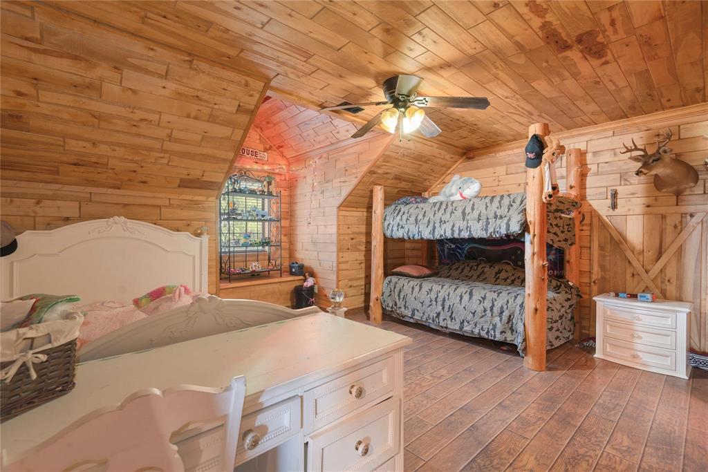 Room featuring natural wood plank walls and ceiling, exposed timber support posts, a built-in recessed shelving nook, and a ceiling fan with integrated lighting