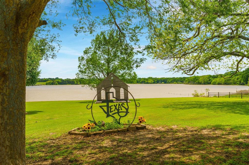 Expansive waterfront acreage featuring a manicured lawn, mature trees, a metal-framed garden bed, and a wooden open-air structure