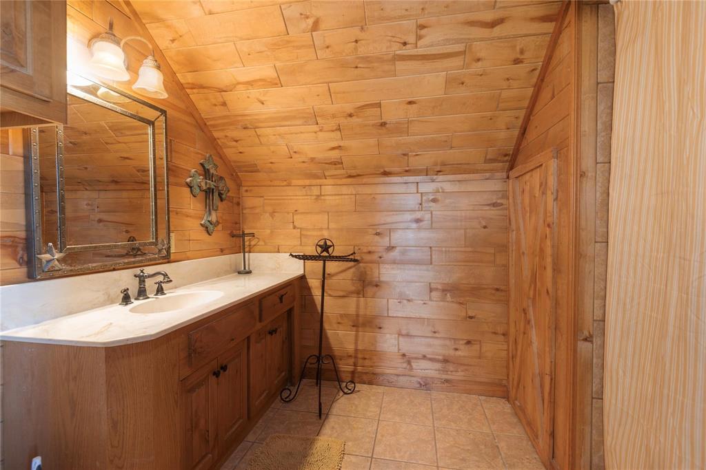 Wood-paneled walls and ceiling, custom cabinetry vanity with an integrated basin, stone-surface countertop, and ceramic tile flooring