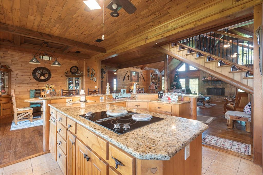 Kitchen island featuring stone countertops, integrated cooktop, and wooden cabinetry, complemented by timber-plank wall paneling and an open staircase with decorative metal railing