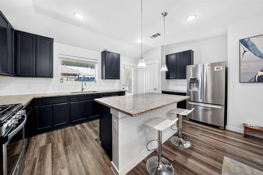 Kitchen featuring dark cabinetry, light countertops, wood-finish flooring, stainless steel appliances, and an island with pendant lighting