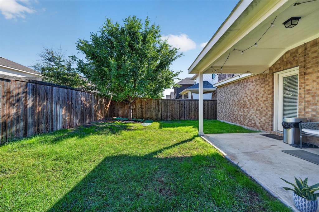 Spacious backyard oasis featuring a mature shade tree, manicured lawn, and wooden privacy fencing