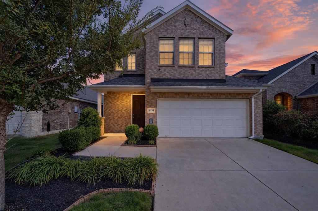 Brick Colonial two-story home featuring a welcoming front elevation with multiple upper-level windows, illuminated entry vestibule, and a wide concrete driveway Brick Colonial two-story home featuring a welcoming front elevation with multiple upper-level windows, illuminated entry vestibule, and a wide concrete driveway