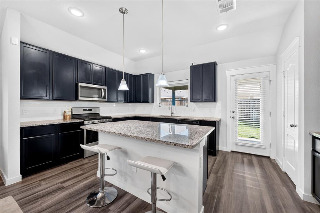 Modern kitchen featuring black cabinetry with stainless steel appliances, granite countertops, a white kitchen island with seating, pendant lighting, recessed ceiling lights, and wood-finish flooring throughout