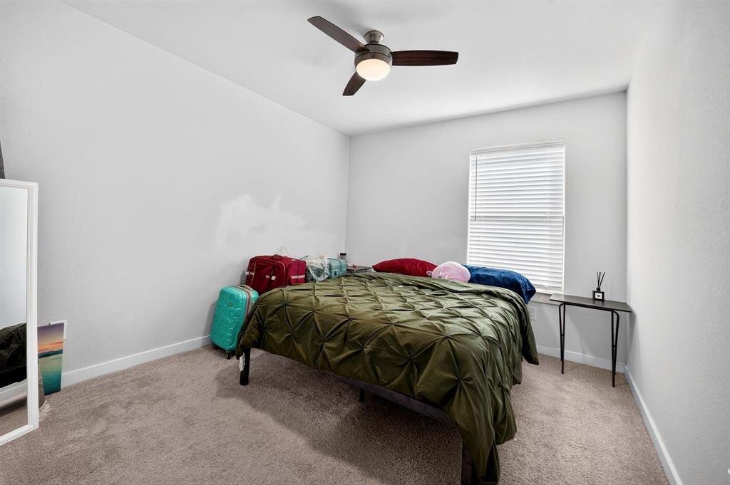 Spacious primary bedroom showcasing rich wood-finish furnishings, neutral carpeting, and abundant natural light from large windows dressed in golden drapery