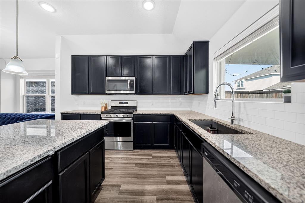 Kitchen featuring dark cabinetry, light-toned countertops, stainless steel appliances, a subway tile backsplash, and wood-finish flooring