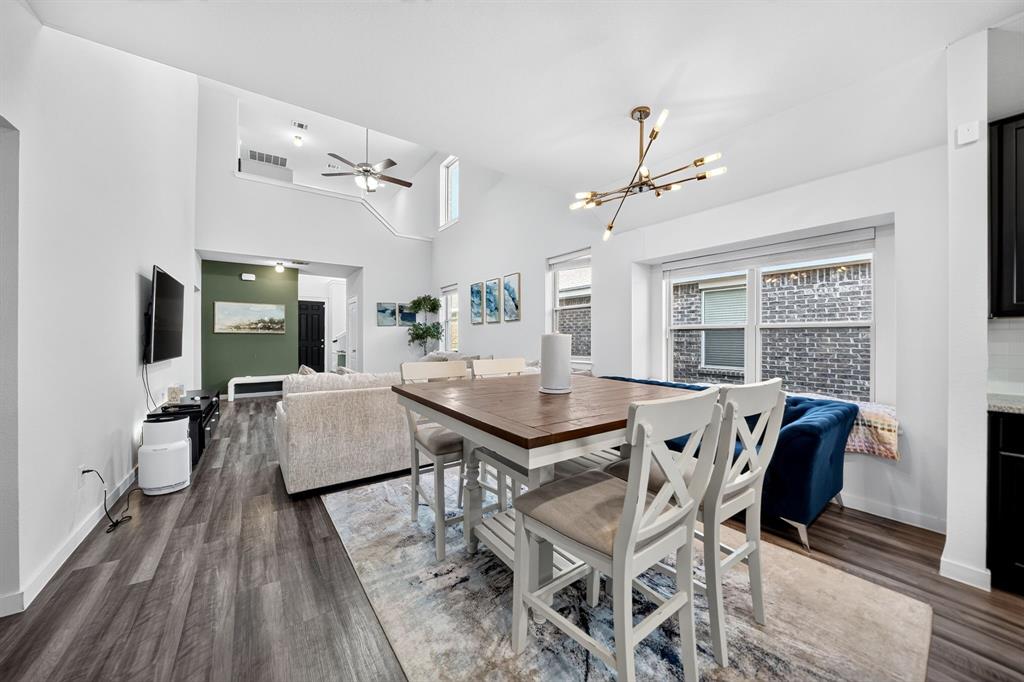 Open-concept dining and kitchen area featuring wood-finish flooring throughout, a dining table with seating for multiple guests, modern pendant lighting, and abundant natural light from large windows