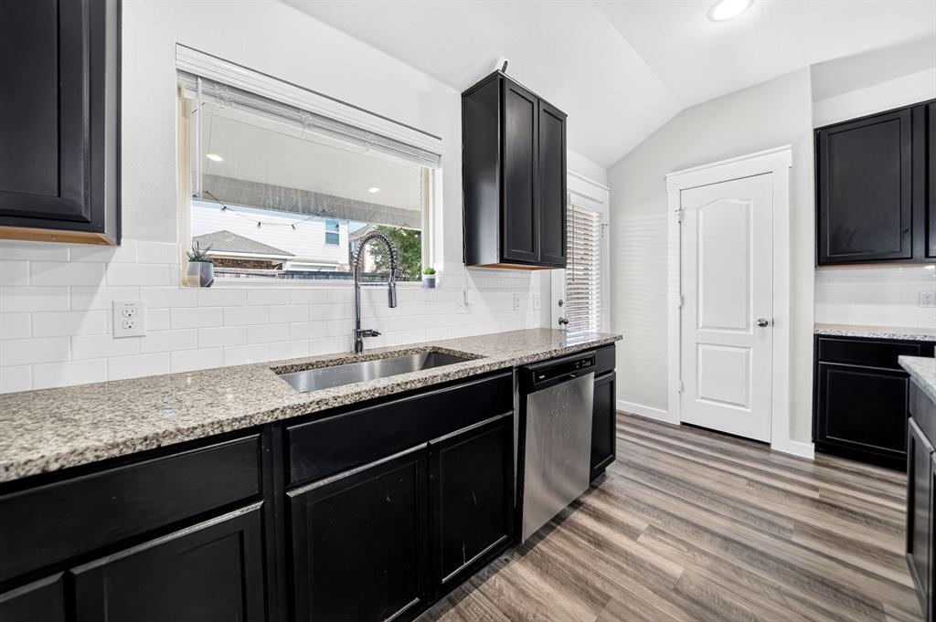 Modern kitchen featuring sleek black cabinetry with brushed nickel hardware, granite countertops, stainless steel appliances including a professional-style faucet, white subway tile backsplash, and wood-finish plank flooring throughout the space