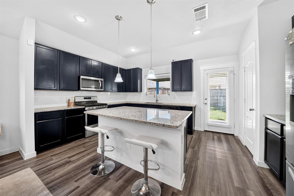 Modern kitchen featuring dark cabinetry with stainless steel appliances, white quartz countertops, a center island with seating, pendant lighting, and wood-finish flooring throughout the open layout