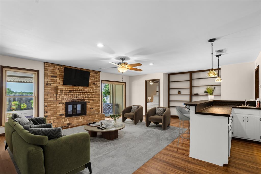 Virtually Staged Living area featuring a brick fireplace, wood-finish flooring, built-in shelving, and a wet bar with pendant lighting