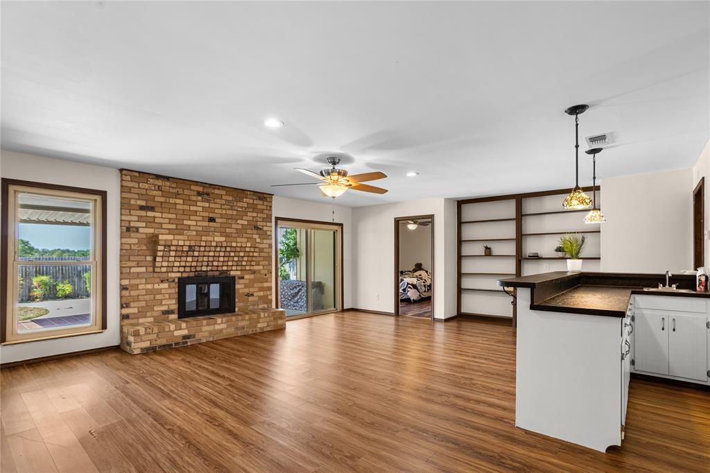 Wood-finish flooring throughout, brick fireplace, built-in shelving, white cabinetry, and sliding glass door