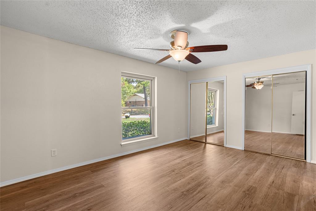 Wood-finish flooring, a window offering exterior views, a ceiling fan with integrated lighting, and mirrored sliding closet doors