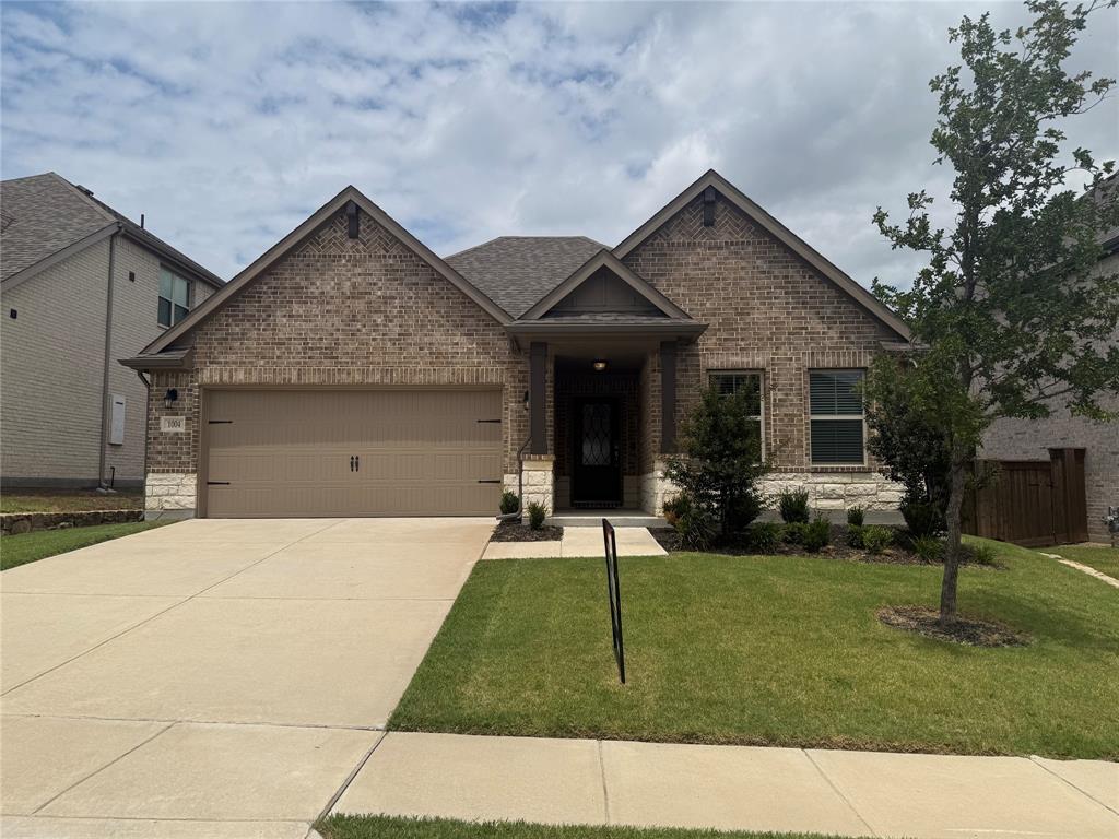 Brick and stone facade with a covered entry, attached two-car garage, and concrete driveway