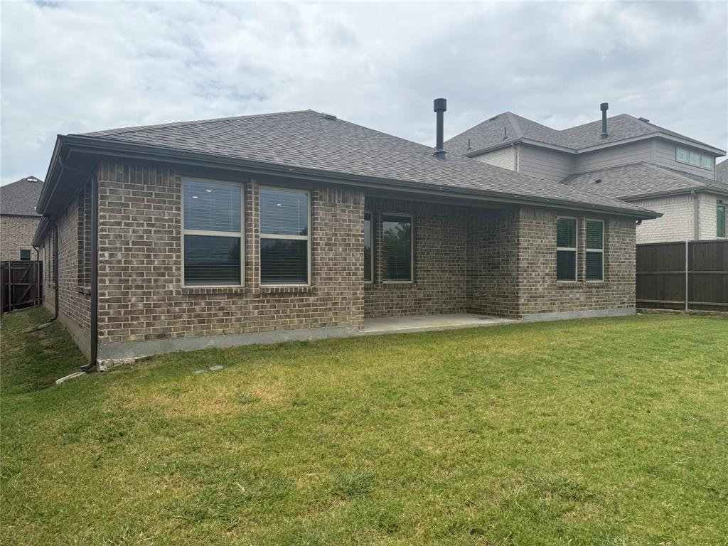 Brick exterior with shingle roofing, featuring a covered concrete patio and a lush lawn