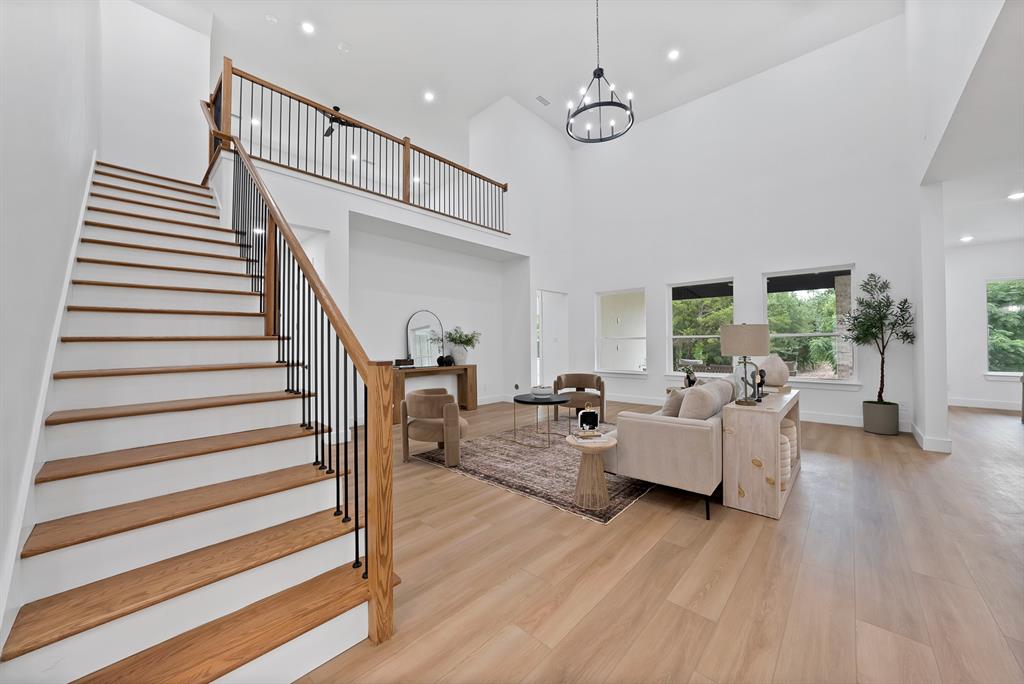 Two-story living area with high ceilings, wood-finish flooring, and an open staircase with a wood handrail and black metal spindles Two-story living area with high ceilings, wood-finish flooring, and an open staircase with a wood handrail and black metal spindles