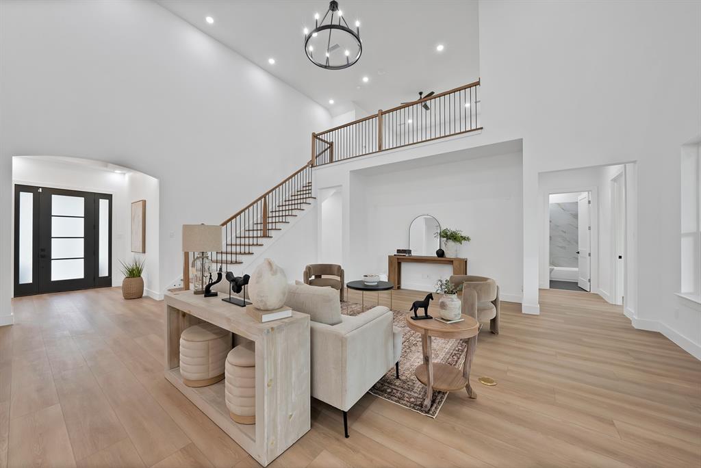 Two-story entry foyer with a dark-framed glass paneled door, wood-finish flooring, and a staircase featuring dark wood treads and a black metal railing