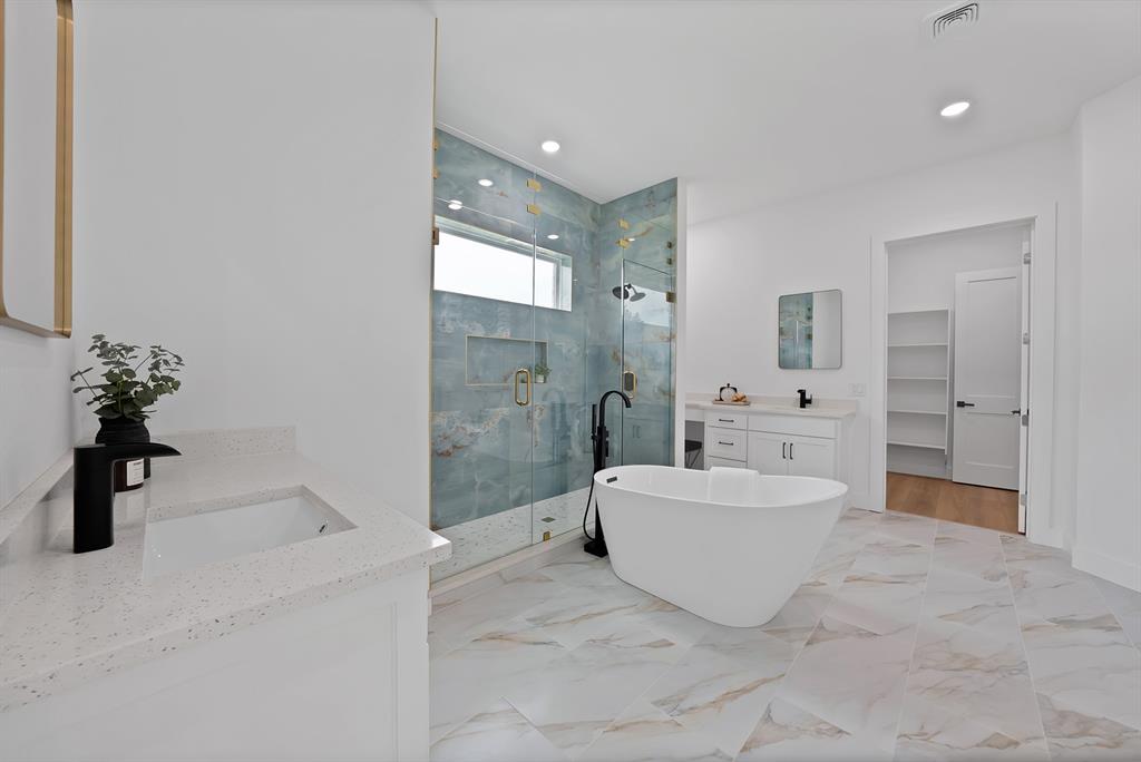 Freestanding soaking tub, walk-in shower with glass enclosure, dual vanity sinks with quartz countertops, and large format tile flooring