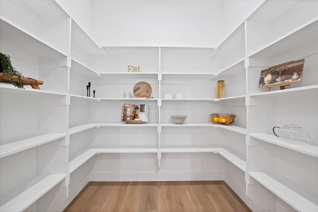 Expansive pantry with extensive white shelving, wood-finish flooring, and bright illumination