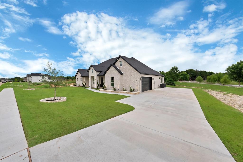 Contemporary exterior featuring light-colored brick, dark roof, dark garage door, extensive concrete driveway, and a manicured lawn Contemporary exterior featuring light-colored brick, dark roof, dark garage door, extensive concrete driveway, and a manicured lawn