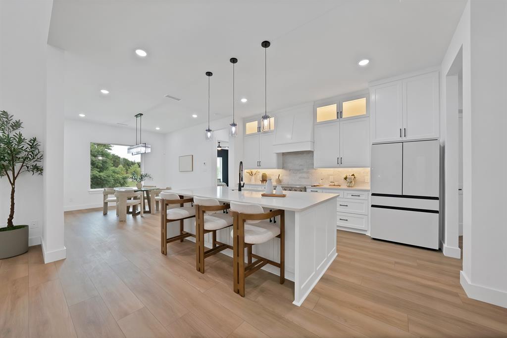 Kitchen featuring a large central island, white cabinetry, integrated appliances, wood-finish flooring, and recessed lighting